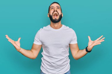 Sakallı, sıradan beyaz tişörtlü genç adam deli gibi bağırıyor, agresif bir ifadeyle bağırıyor ve kollarını kaldırıyor. hüsran kavramı. 