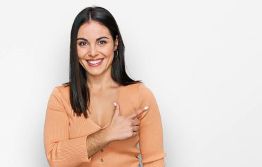 Gündelik kıyafetler giyen, neşeli, yüzünde bir gülümseme olan genç İspanyol kadın mutlu ve doğal bir ifadeyle elini ve parmağını kaldırdı. 