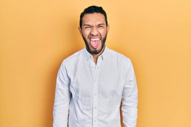 Hispanic man with beard wearing business shirt sticking tongue out happy with funny expression. emotion concept. 