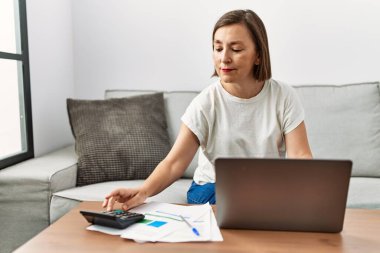 Orta yaşlı İspanyol kadın ev işlerinde ev işleri için dizüstü bilgisayar kullanıyor.