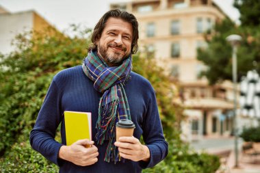 Orta yaşlı yakışıklı bir adam parkta bir fincan kahve içiyor.