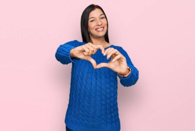 Gündelik kıyafetler giyen, aşık gülümseyen, elleriyle kalp sembolü yapan genç İspanyol kadın. romantik kavram. 