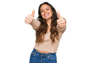 Latin asıllı genç bir kız günlük giysiler giyip olumlu jestler yapıyor. Elleriyle gülümsüyor ve başarı için seviniyor. kazanan jest. 