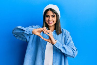 Sevimli yün şapka takan, aşık olmuş genç Latin kadın elleriyle kalp sembolü yapıyor. romantik kavram. 