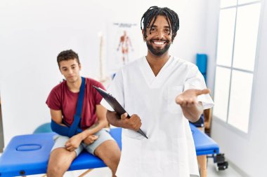 Kırık kollu, gülümseyen, yardım eli uzatan ve kabul gören bir adamla birlikte acı giderme kliniğinde çalışan genç İspanyol bir adam.. 