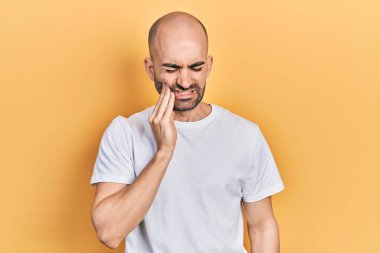 Dişlerinin ağrıması ya da diş hastalığından dolayı günlük beyaz t-shirt giyen genç kel bir adam ağızlarına acı dolu bir ifadeyle dokunuyor. dişçi 