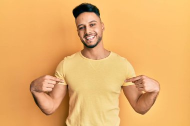 Gündelik giysiler giyen genç bir Arap. Kendine güvenen, gülümseyen, kendini gururlu ve mutlu gösteren bir adam.. 