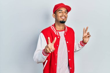 Young african american man wearing baseball uniform smiling looking to the camera showing fingers doing victory sign. number two. 