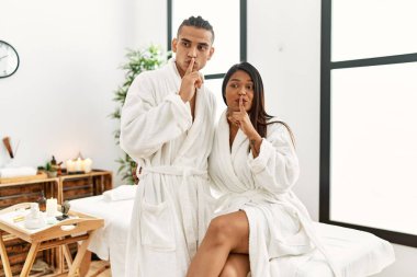 Havlu giymiş genç Latin bir çift güzellik merkezinde durup parmakları dudaklarında sessiz olmak istiyorlar. sessizlik ve gizli konsept. 