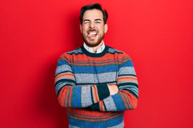 Kollarını kavuşturmuş, sakallı, yakışıklı beyaz adam. Komik bir ifadeyle dilini dışarı çıkarıyor.. 