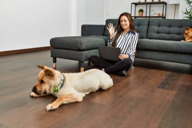 Genç İspanyol kadın evde köpeklerle yerde otururken görüntülü konuşma yapıyor.