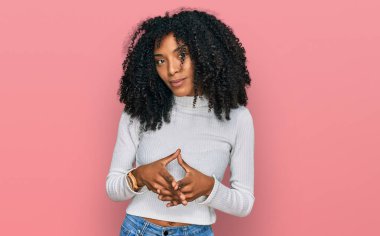 Genç Afro-Amerikalı kız, günlük giysiler içinde ellerini birleştirip gülümseyerek rahat ve neşeli gülümsüyor. Başarı ve iyimserlik 
