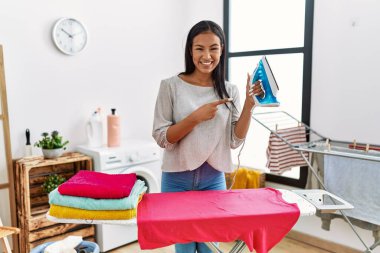 Giysilerini ütüleyen genç İspanyol kadın gülümseyerek el ve parmağıyla işaret ediyor. 