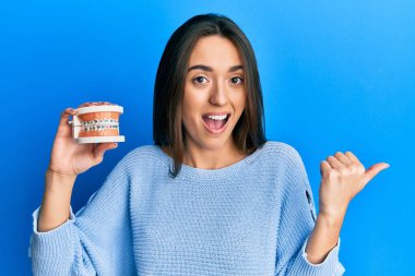 Genç İspanyol kız ortodontik parmağıyla baş parmağını kaldırıyor ve ağzı açık gülümsüyor. 