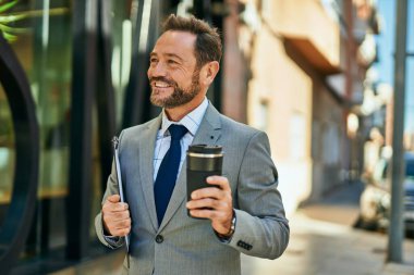 Orta yaşlı işadamı gülümseyerek şehirde kahve içiyor..