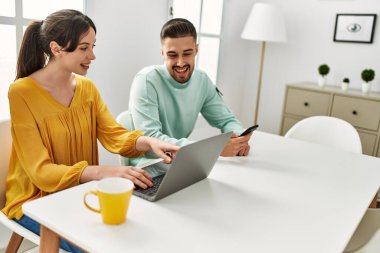 Laptop ve akıllı telefon kullanan genç İspanyol çift evde kahve içiyor..