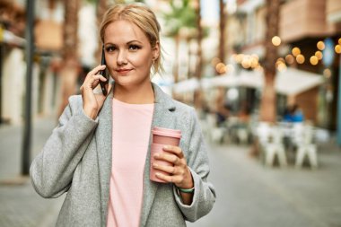 Sarışın iş kadını akıllı telefondan konuşuyor. Şehirde kahve içiyor..