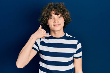 Handsome young man wearing casual striped t shirt smiling doing phone gesture with hand and fingers like talking on the telephone. communicating concepts. 