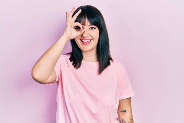 Gündelik kıyafetler giyen genç İspanyol kadın el hareketleriyle gülümsüyor ve mutlu yüzüyle parmaklarının arasından bakıyor.. 