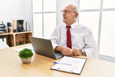 Senior man working at the office using computer laptop smiling looking to the side and staring away thinking. 