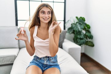 Genç sarışın kadın adet bardağını tutuyor. Gülümsüyor, mutlu bir şekilde elini ve parmağını yana uzatıyordu. 