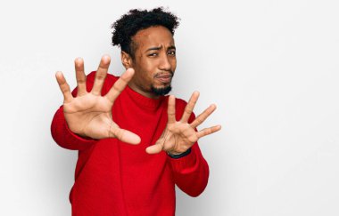 Young african american man with beard wearing casual winter sweater afraid and terrified with fear expression stop gesture with hands, shouting in shock. panic concept. 