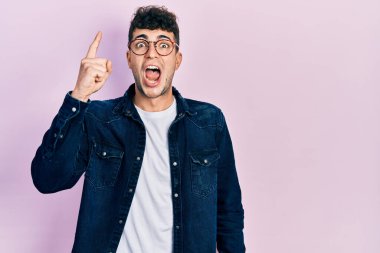 Gündelik kıyafetler giyen ve gözlüklü genç İspanyol başarılı bir fikirle işaret ediyor. Heyecanlı ve mutlu. Bir numara.. 