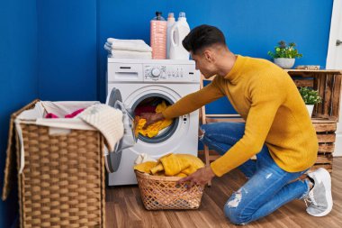 Young hispanic man washing clothes at laundry