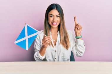 İskoç bayrağını elinde tutan genç bir kadın masaya oturmuş gülümsüyor bir fikir veya soru işareti ile mutlu bir yüzle, bir numara 