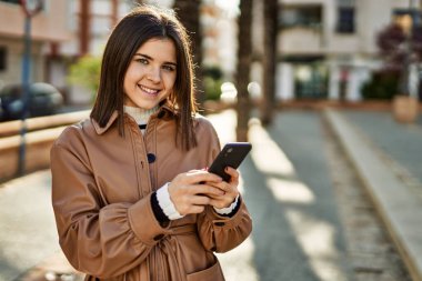 Genç, güzel esmer kadın dışarıda mutlu bir şekilde gülümsüyor akıllı telefon kullanıyor.