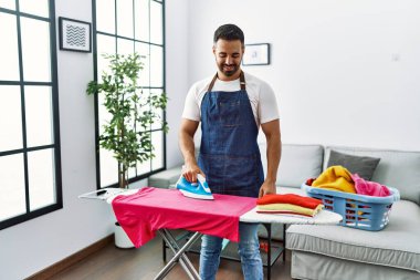 Genç İspanyol adam gülümsüyor. Evde kendine güvenen ütü yapıyor.