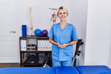 Acıyı dindirme kliniğinde çalışan genç fizyoterapist kadın ellerini birleştirip gülümsüyor. Başarı ve iyimserlik 