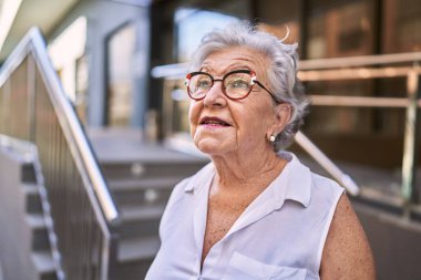 Yaşlı, kır saçlı, gülümseyen bir kadın sokakta kendine güveniyor.