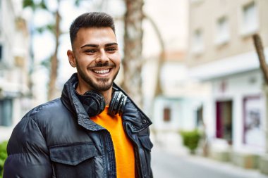 Sakallı yakışıklı, neşeli ve kendine güvenen, kışlık palto ve kulaklık takan bir İspanyol.