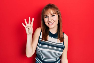 Kızıl saçlı genç kadın, gündelik tişört giyip parmaklarıyla dört numarayı gösterirken kendinden emin ve mutlu bir şekilde gülümsüyor.. 