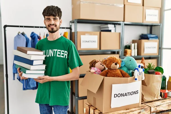 Jonge Spaanse Man Vrijwilligersuniform Met Boeken Een Liefdadigheidscentrum — Stockfoto