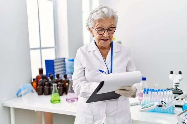 研究室のクリップボードに科学者の制服を着たシニア白髪の女性 — ストック写真
