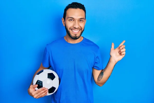 Hispanic Man Beard Holding Soccer Ball Cheerful Smile Face Pointing — Stok fotoğraf
