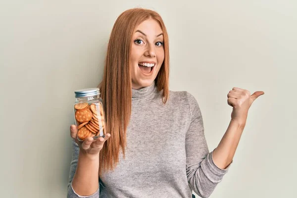 Young Irish Woman Holding Jar Salty Biscuits Pointing Thumb Side — Stock Fotó