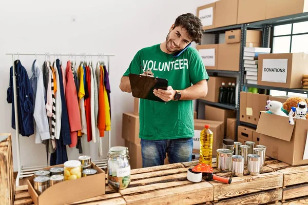 Jonge Spaanse Man Draagt Vrijwilliger Uniform Schrijven Klembord Praten Smartphone — Stockfoto