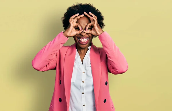 ビジネスジャケットを着たアフロヘアのアフリカ系アメリカ人女性は 双眼鏡の舌を突き出すようなOkジェスチャーを行い 目は指を通して見る クレイジーな表現 — ストック写真