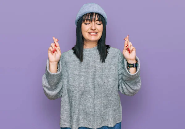 Young Hispanic Woman Wearing Cute Wool Cap Gesturing Finger Crossed — Stock Photo, Image