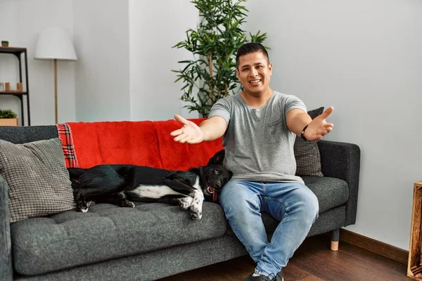 Jovem Latino Homem Cão Sentado Sofá Casa Sorrindo Alegre Oferecendo — Fotografia de Stock