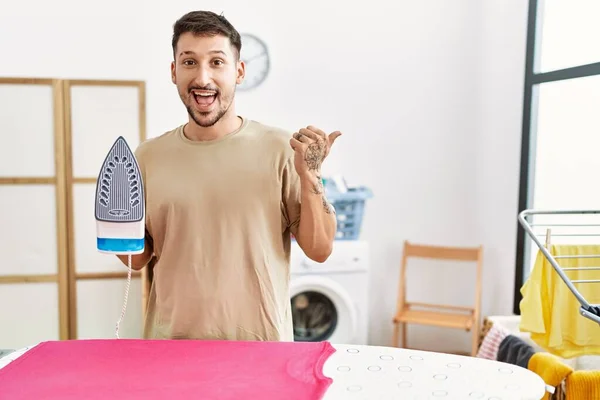 Jovem Homem Bonito Passar Roupas Casa Apontando Polegar Para Lado — Fotografia de Stock