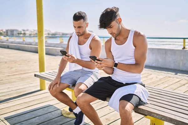 Dos Hombres Hispanos Pareja Deportiva Usando Teléfono Inteligente Sentado Banco —  Fotos de Stock