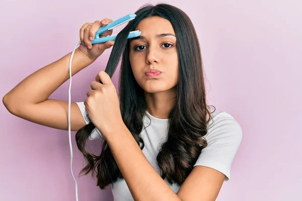 Young Hispanic Woman Holding Hair Straightener Puffing Cheeks Funny Face — Stockfoto