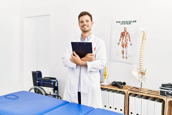 Young Hispanic Man Wearing Physiotherapist Uniform Holding Clipboard Clinic — Stok fotoğraf