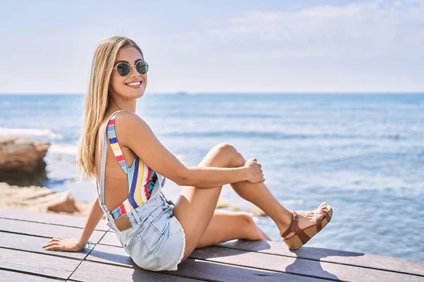 年轻的金发姑娘高兴地坐在海滩的长椅上 — 图库照片