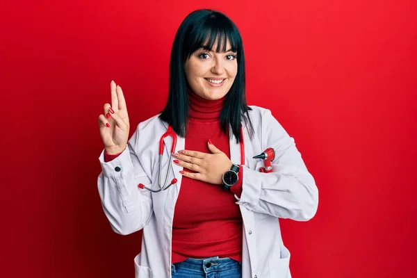 Young hispanic woman wearing doctor uniform and stethoscope smiling swearing with hand on chest and fingers up, making a loyalty promise oath