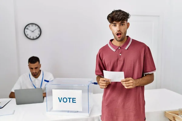 投票箱に封筒を入れて若いヒスパニック系の男が怖がって驚きのために口を開けて驚いて 不信の顔 — ストック写真